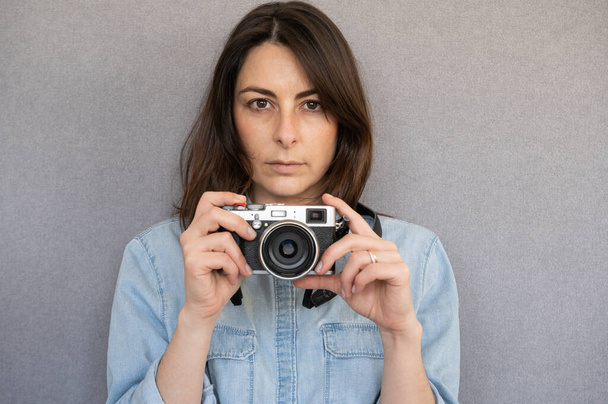 Vooraanzicht van portret van mooie en jonge vrouw met een vintage stijl camera.Isolated op grijze achtergrond - Foto, afbeelding