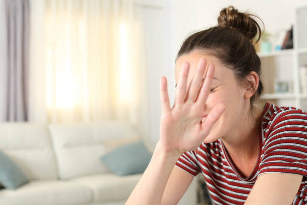 Embarrassed woman avoiding photo shoot covering face with her hand in the living room at home - Fotoğraf, Görsel