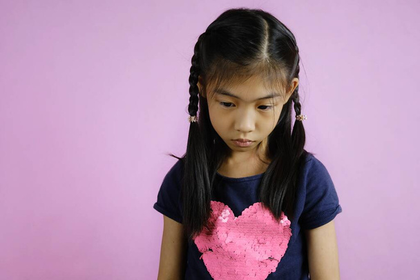 Μια φωτογραφία μισού σώματος ενός χαριτωμένου κοριτσιού από την Ασία να κοιτάει κάτω, να νιώθει αναστατωμένη, να σκέφτεται την επόμενη δράση της. Φωτεινό ροζ φόντο. - Φωτογραφία, εικόνα
