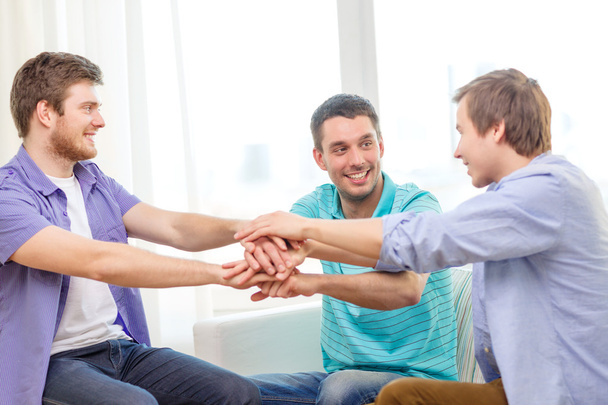 smiling male friends with hands together at home - Zdjęcie, obraz
