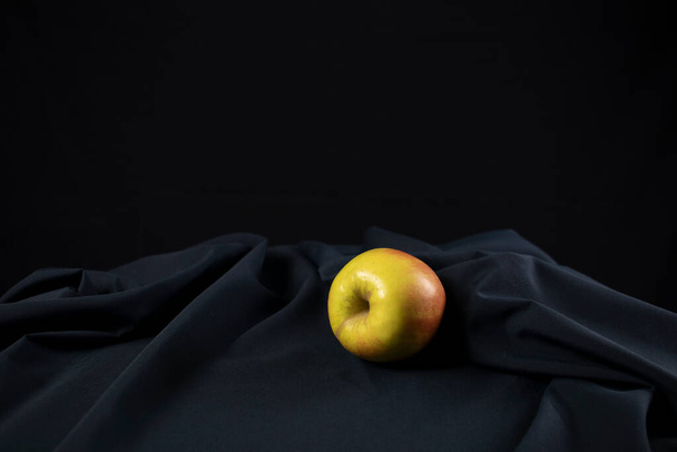 A beautiful yellow apple with red sides lies on a dark tablecloth. Black background. Close-up. - 写真・画像
