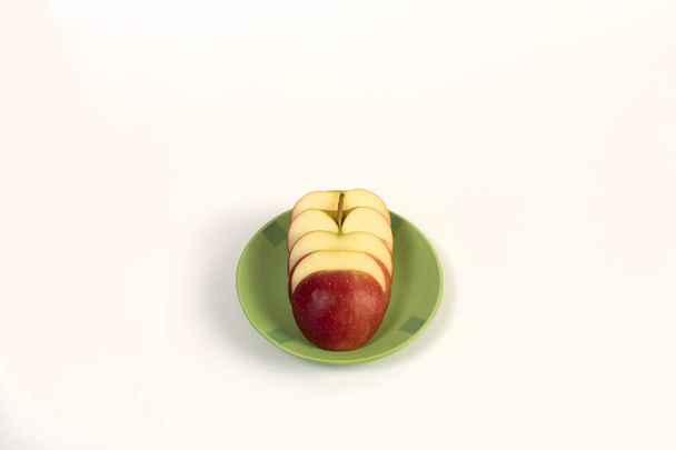 Flache Scheiben eines roten, reifen Apfels liegen auf einer grünen Untertasse. Nahaufnahme. Weißer Hintergrund. - Foto, Bild