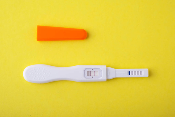 Sarı arka planda pozitif hamilelik testi. Üst görünüm - Fotoğraf, Görsel
