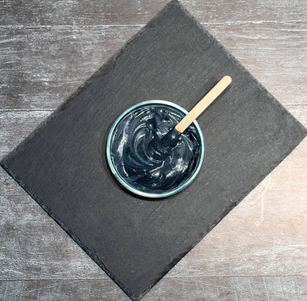 Homemade face mask and scrub with activated charcoal powder and yogurt with stick on black slate platter. - Photo, Image