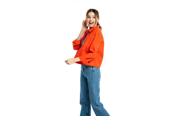 verbaasd jonge vrouw in jeans, gewas top en oranje shirt geïsoleerd op wit  - Foto, afbeelding
