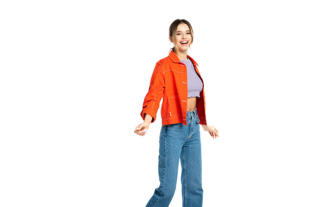 excited young woman in jeans, crop top and orange shirt isolated on white  - 写真・画像