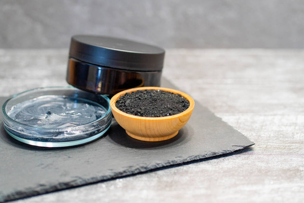 Homemade face mask and scrub with activated charcoal powder and yogurt with stick on black slate dish with jar. - Foto, Bild