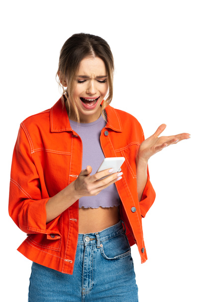 displeased young woman in crop top and orange shirt using smartphone and gesturing  isolated on white - Fotografie, Obrázek