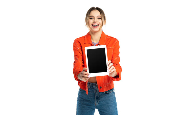 cheerful young woman in orange shirt and jeans holding digital tablet with blank screen isolated on white - Foto, afbeelding
