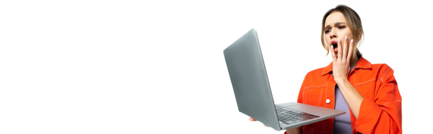 geschokte vrouw in oranje shirt kijken naar laptop geïsoleerd op wit, banner - Foto, afbeelding