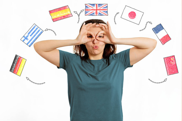 Angol Nyelvnap. Egy nő arcképe, amint egy vicces grimaszt vág az arcára. Fehér háttér különböző országok zászlóival. Az idegen nyelvek tanulásának koncepciója. - Fotó, kép
