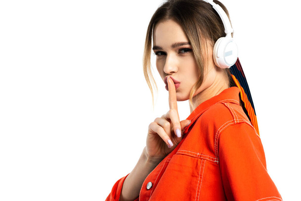 woman in orange shirt listening music in wireless headphones and showing hush sign isolated on white - Фото, зображення