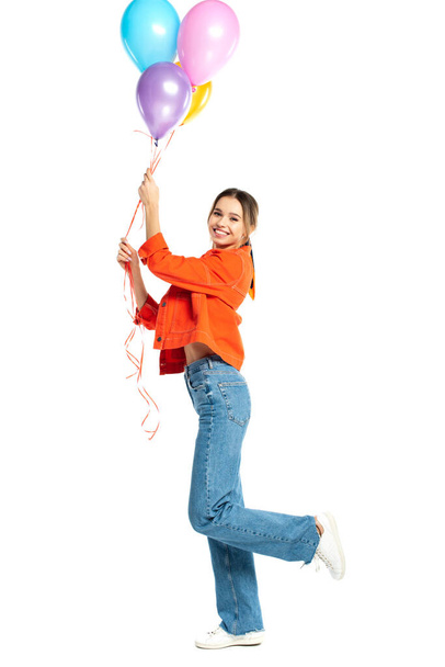 volledige lengte van vrolijke jonge vrouw in oranje shirt met kleurrijke ballonnen geïsoleerd op wit - Foto, afbeelding