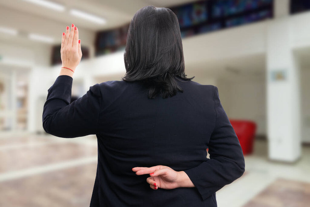 Empresaria corporativa con traje de trabajo casual haciendo un gesto de juramento falso con los dedos cruzados detrás de la espalda y la palma hacia arriba - Foto, imagen