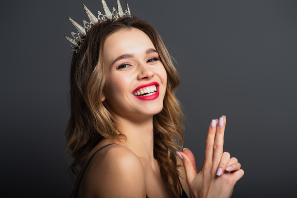 happy woman in tiara with diamonds showing gun gesture with hands on grey - Foto, Imagen