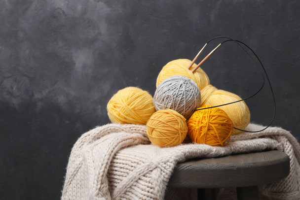 Woolen yarns with knitting needles and scarf on stand near black wall. Space for text - Photo, Image