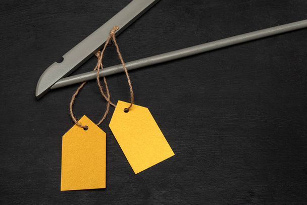 Wooden hanger with yellow paper labels. Black background. Blank label mockup . Clothing tag. - Photo, Image