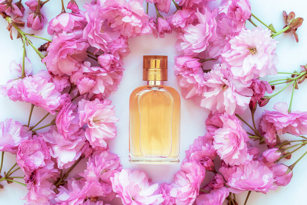 ピンクの桜の花を背景に香水瓶。美容化粧品、スキンケア。トップビュー、フラットレイアウト. - 写真・画像