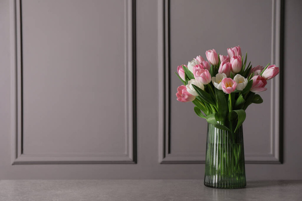 Beautiful bouquet of tulips in glass vase on grey table. Space for text - Fotó, kép