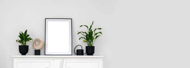 Panoramiczny widok roślin domowych, konewka do kwiatów, ramka i wazon stojący na półce nad białym kominkiem vintage. Przytulne mieszkanie ze ścianą ksero. Nowoczesna koncepcja wnętrz - Zdjęcie, obraz