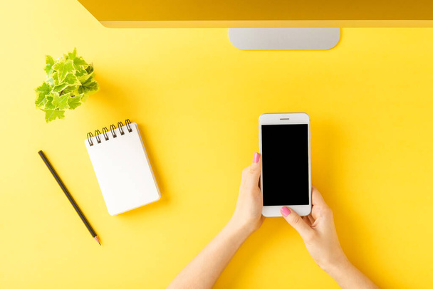 Woman hands using mobile phone with empty screen on yellow table. Office desktop concept. Top view - Foto, immagini