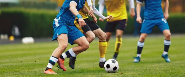 若い大人のサッカー選手はピッチで競争する。サッカーリーグの試合。ジャージーシャツとクリーツの十代のスポーツ選手キック黒と白のサッカーボール - 写真・画像