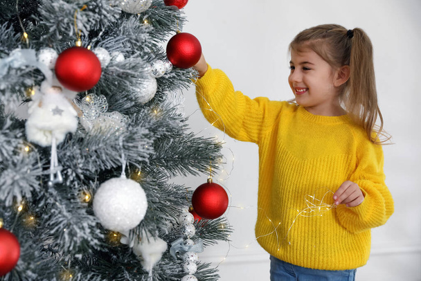 Cute little girl decorating Christmas tree at home - 写真・画像