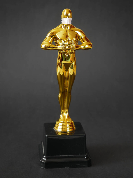 Estatua del premio Oscar de oro de Hollywood en máscara médica. Concepto de éxito y victoria. Ceremonia Oscar en tiempo del coronavirus - Foto, Imagen