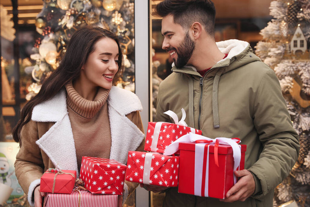 Lovely couple with presents near store decorated for Christmas outdoors - 写真・画像