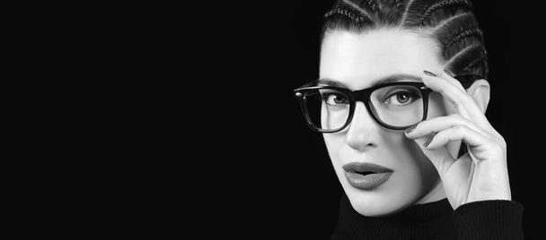 Monocromo hermosa mujer joven con estilo con pelo trenzado llevar gafas o anteojos. Concepto de cuidado de la visión, optometría y moda, aislado sobre fondo negro - Foto, Imagen