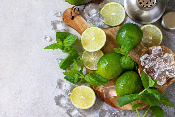 Refreshing cold summer Mojito cocktail making. Mint, lime, ice ingredients and bar utensils on a stone or concrete table. Top view flat lay. Copy space. - Foto, afbeelding