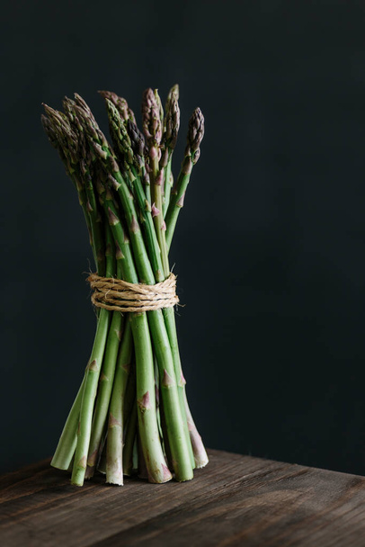 Bunch of raw fresh asparagus on wooden table against black background. - Фото, изображение