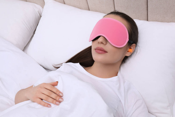 Kulak tıkacı ve maskesiyle yatakta uyuyan genç bir kadın. - Fotoğraf, Görsel