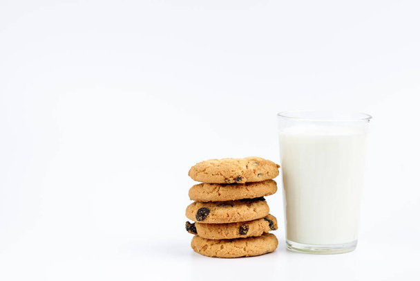 Een glas melk en koekjes met rozijnen op een witte achtergrond - Foto, afbeelding