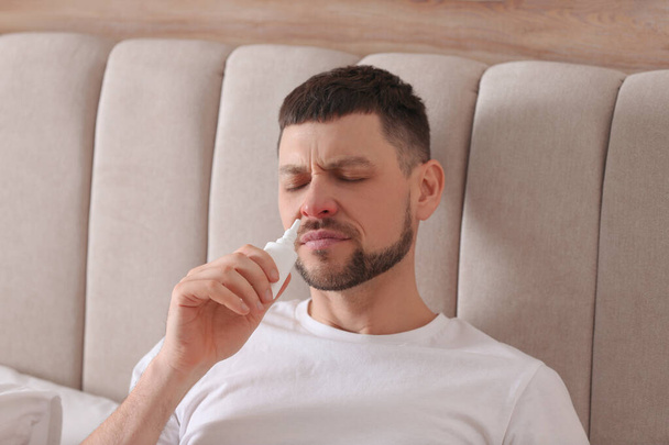 Ill man using nasal spray in bed at home - Foto, afbeelding
