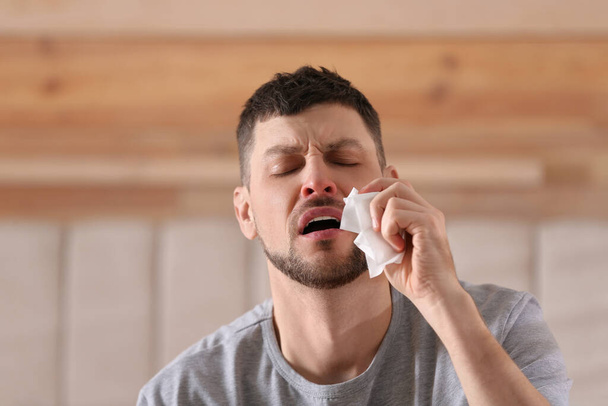 Ill man with paper tissue sneezing at home - Zdjęcie, obraz