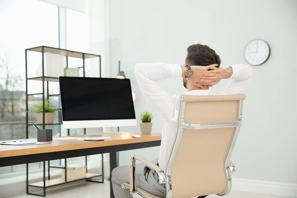 Young businessman relaxing in office chair at workplace, back view. Space for text - Foto, immagini