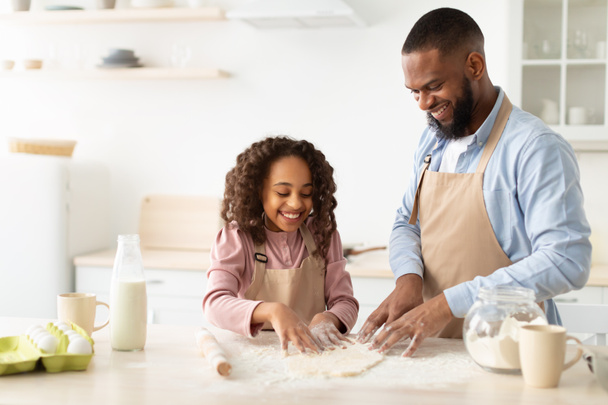 Cheerful afro man and his child daughter kneading dough - Foto, Bild