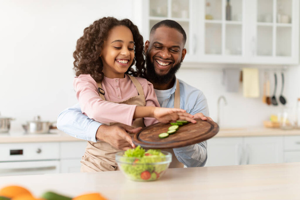 Fröhlicher Afro-Vater und Tochter kochen gemeinsam Salat - Foto, Bild