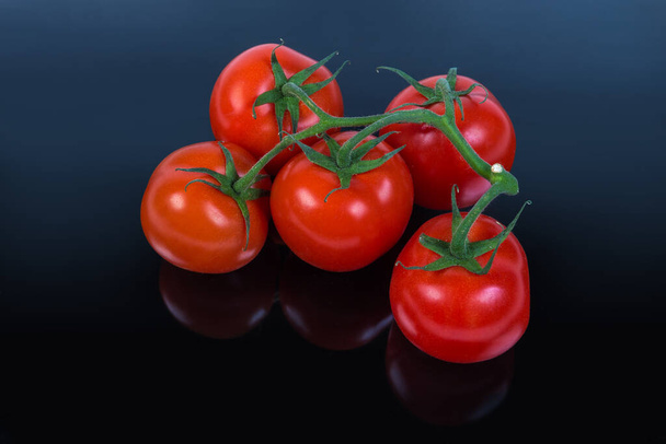 Branch of the ripe red tomatoes on a dark matt reflective surface - Photo, Image