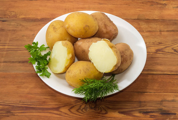 Ziemniaki gotowane w skórkach z gałązkami zieleni na białym talerzu na starym rustykalnym stole - Zdjęcie, obraz