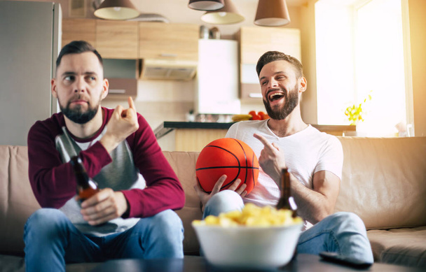 Two excited funny young friends fans of basketball watching TV match and shouting while resting on the couch - Фото, зображення