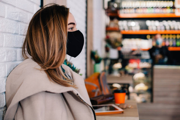 Young girl in protective mask sits in a coffee shop waiting for a drink - Foto, Bild