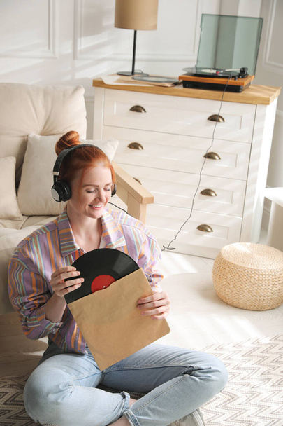 Young woman listening to music with turntable in living room - Foto, imagen