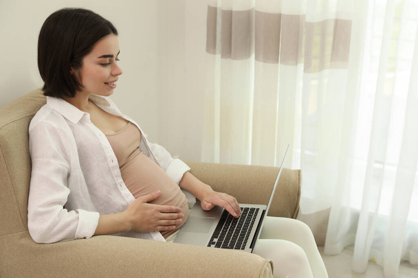 Pregnant young woman with laptop at home, space for text - Fotó, kép