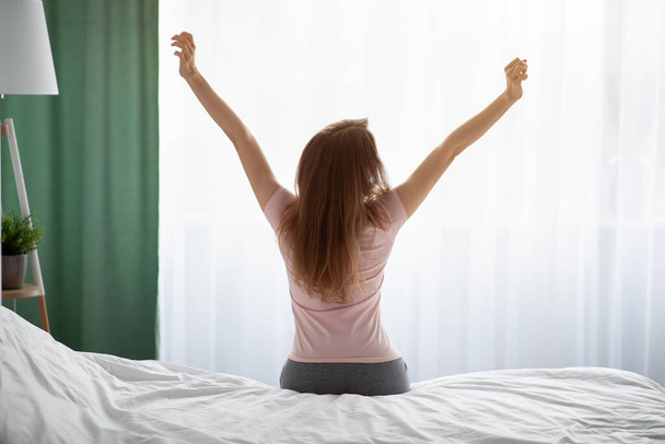 Visszapillantás fiatal nő nyújtózkodik az ágyon, miután felébredt otthon - Fotó, kép