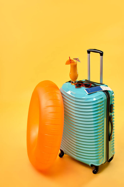 スーツケース、カクテル、チケットとゴムリングは黄色の背景に隔離されています。レクリエーション、旅行、観光の概念。レジャーアクセサリー. - 写真・画像