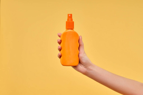 Woman's hand holds bottle with sunscreen isolated on yellow background. Summer time. Leisure, travel, tourism. - Photo, Image