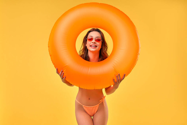 Roztomilá žena v plavkách s gumovým kroužkem izolovaným na žlutém pozadí. Léto. Odpočinek, dovolená, cestování. - Fotografie, Obrázek