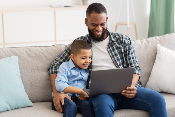 Africano papai abraçando filho sentado com laptop assistindo desenhos animados interior - Foto, Imagem